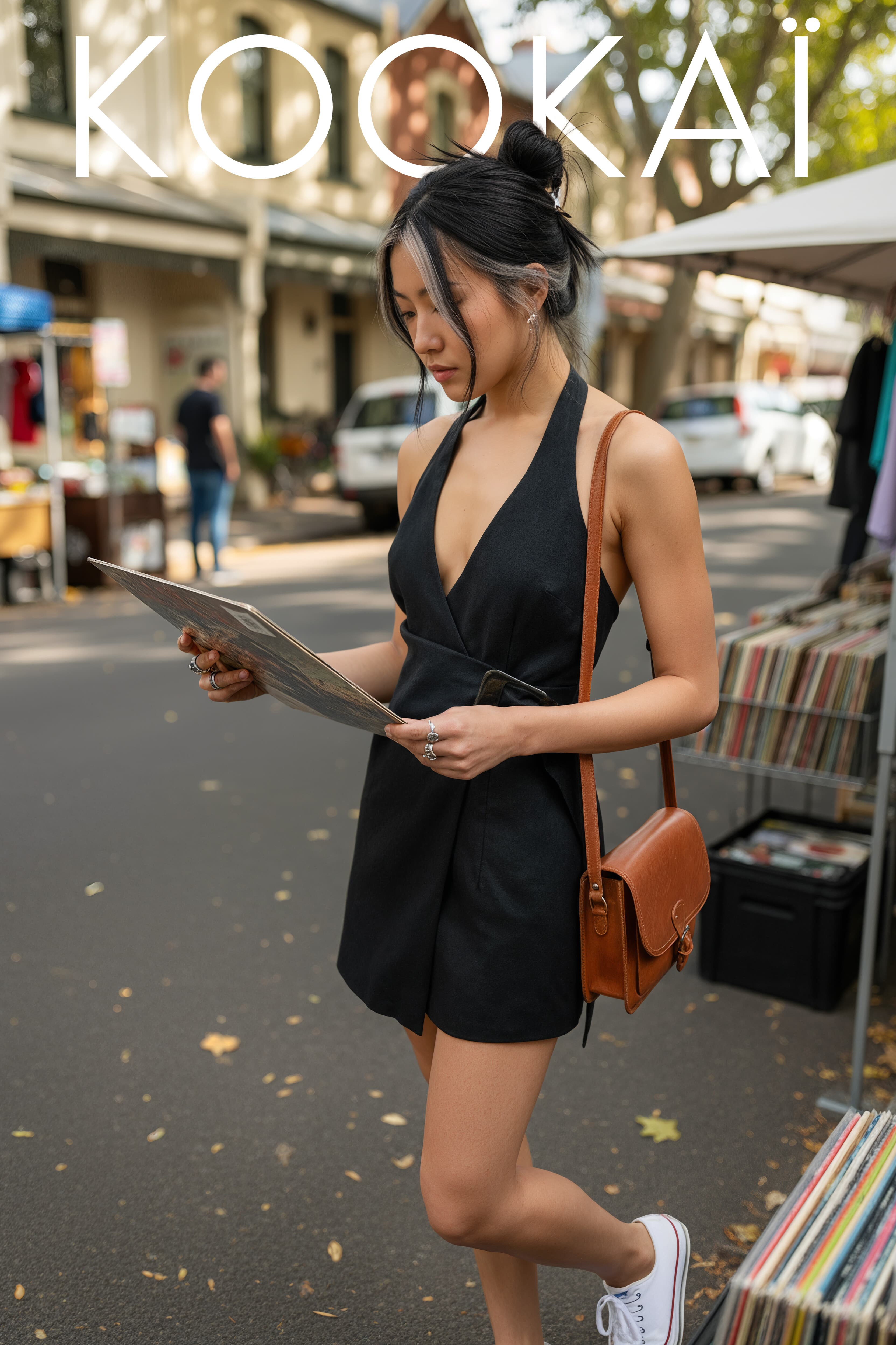 Kookai campaign: model in a black playsuit browsing records at a street market