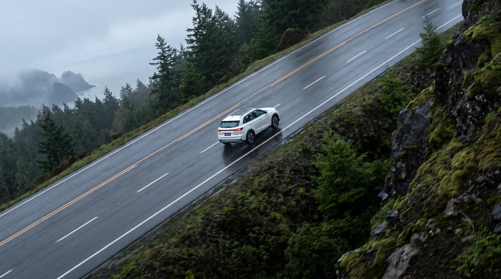 Aerial of a white SUV on a wet forest mountain road