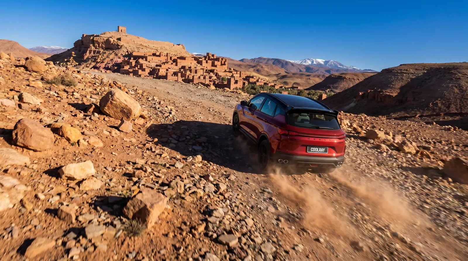 Red SUV descending a rocky trail below an Atlas kasbah