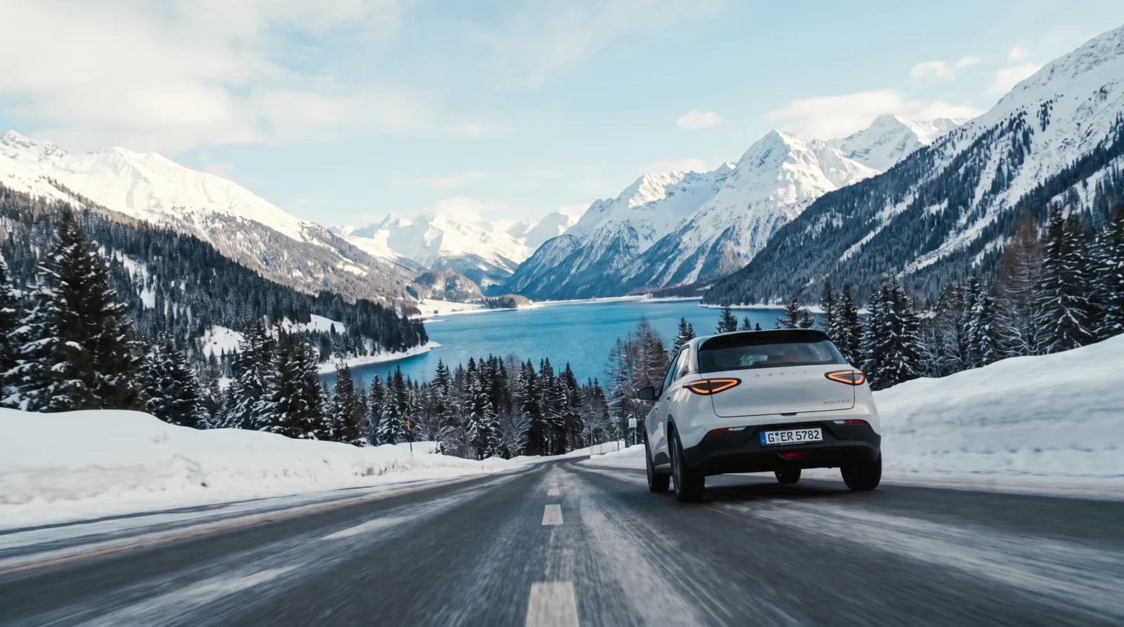 White SUV on a snowbound alpine road above a turquoise lake