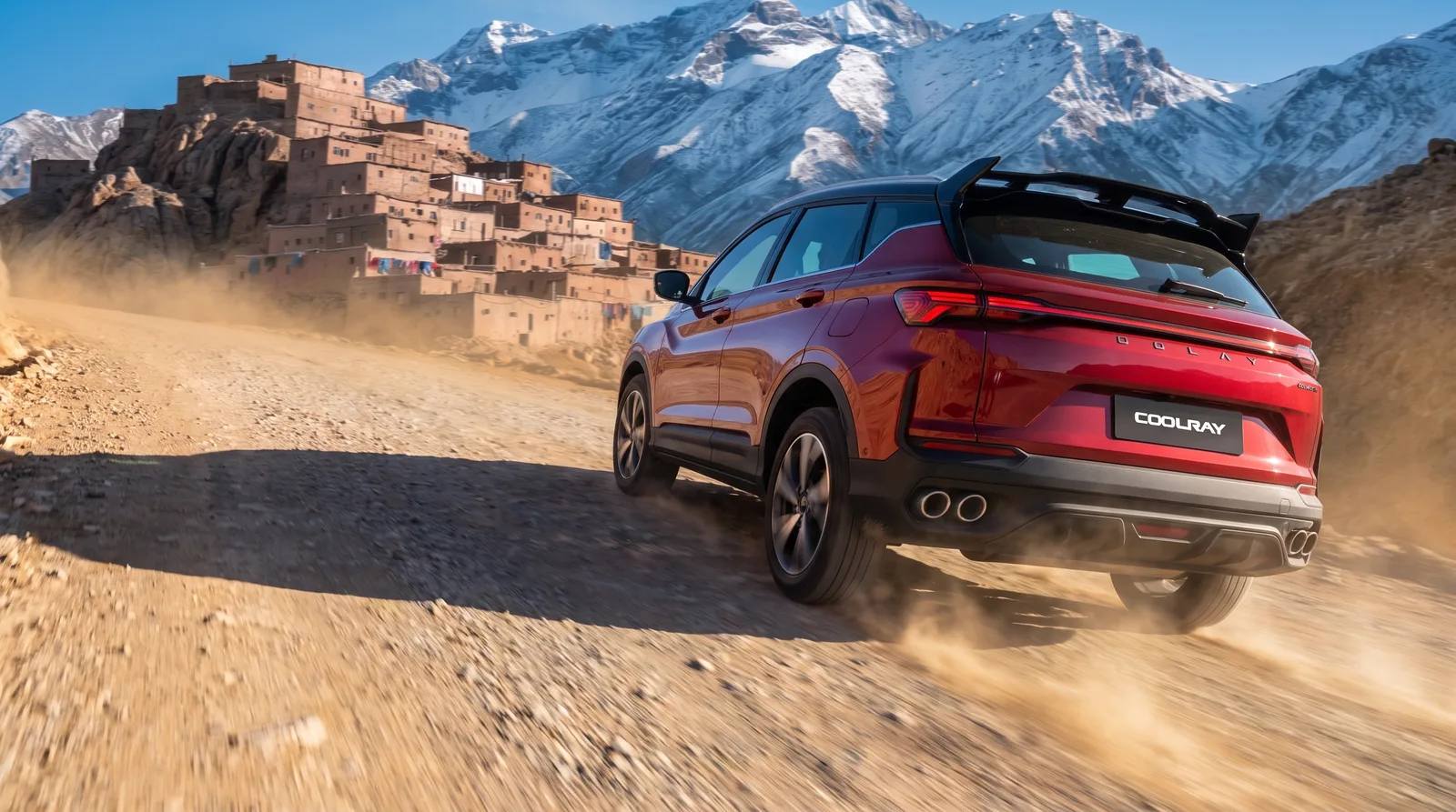 Red Coolray climbing a dusty kasbah road below snow peaks