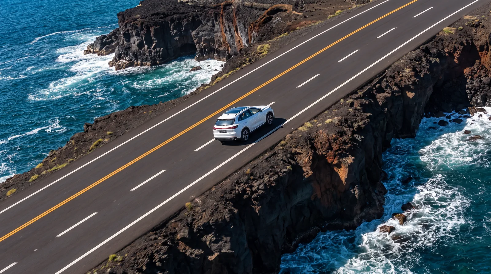 Aerial of a white SUV on a volcanic coast road
